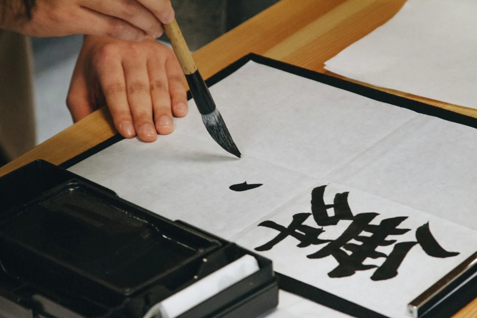 Manos escribiendo un kanji con pincel sobre papel de arroz